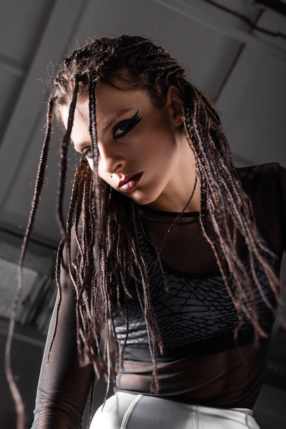 low angle view of futuristic style woman with stylish makeup and dreadlocks on grey background - 写真・画像