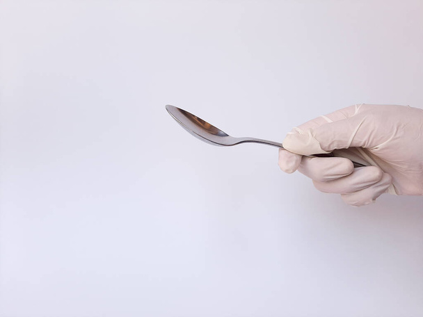 A hand with white latex glove holds metal spoon. Isolated on a white background - Valokuva, kuva