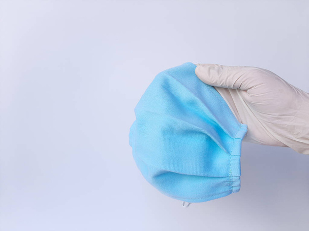 A hand with white latex glove, holds blue mask. Isolated in white background - Photo, Image