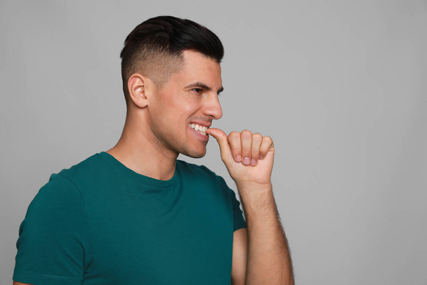 Man biting his nails on grey background. Bad habit - Фото, изображение