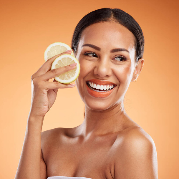 Face, skincare and woman with lemon for health, wellness and vitality on orange studio background. Model, smile and female from Canada with citrus fruit for healthy vitamin c, minerals or nutrition - Fotografie, Obrázek