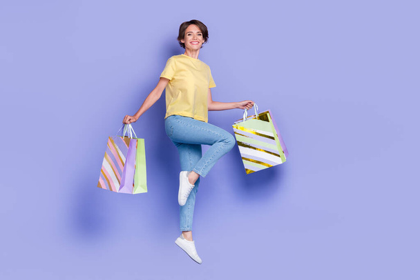 Full length portrait of cheerful energetic person jumping hands hold packages isolated on purple color background. - Foto, immagini