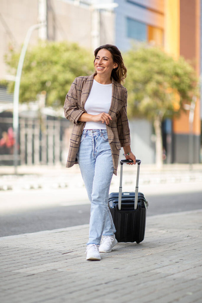 Full body portrait of happy young travel woman pulling suitcase in city  - Foto, Bild