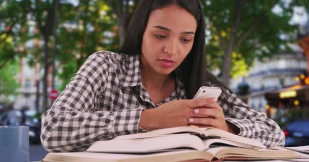 過労したヒスパニック系女性の学生は、クラスで議論された概念について彼女の電話で同級生をテキスト.ストレスラティーナの大学生は、彼女のスマートフォンの彼女の本の中で混乱の概念を検索します。4k - 映像、動画