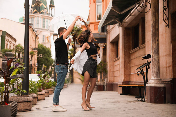Young couple with umbrella dancing under rain on city street - Photo, Image