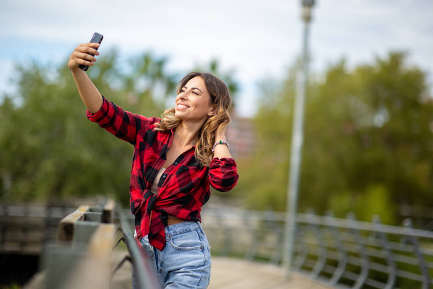 Портрет красивої молодої жінки з мобільним телефоном, що приймає селфі на відкритому повітрі
  - Фото, зображення