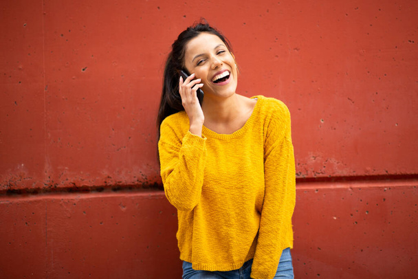 Смеющаяся женщина с телефоном у красной стены - Фото, изображение