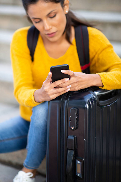 Portrait of young woman holding mobile phone by suitcase  - Fotó, kép