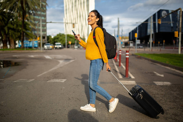 Full body side portrait of young travel woman walking with mobile phone and bag - Photo, Image