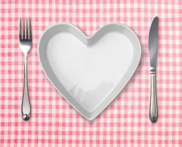 Πίνακας συναντήσεων με σχήμα καρδιάς πλάκα. Πρότυπο με άδειο πιάτο, πιρούνι, μαχαίρι σε ρετρό τραπεζομάντιλο. - Φωτογραφία, εικόνα