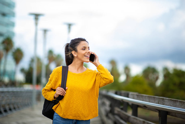 Πορτρέτο του χαμογελαστού νεαρή γυναίκα μιλάμε και το περπάτημα με το κινητό τηλέφωνο στην πόλη - Φωτογραφία, εικόνα