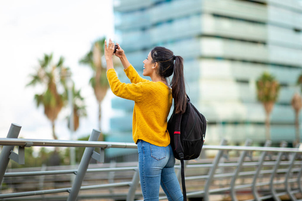 Seitenporträt einer jungen Frau, die mit dem Handy ein Foto von der Stadt macht  - Foto, Bild
