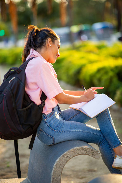 Retrato lateral de una joven hablando con un celular y escribiendo en un libro - Foto, Imagen