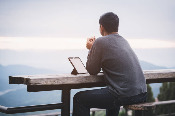 Freelancer τύπος χρησιμοποιώντας tablet φορητό υπολογιστή, ενώ κάθεται και σκέφτεται κατά ορεινό τοπίο κατά τη διάρκεια των διακοπών το καλοκαίρι ταξίδι.Έννοια του ταξιδιού και online εργασίας - Φωτογραφία, εικόνα