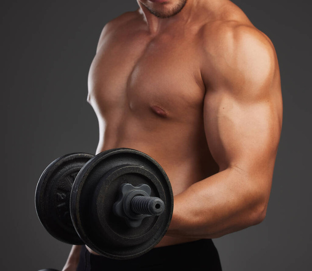 Working on his biceps. an unrecognizable and athletic young man lifting weights while shirtless in studio against a dark background - Foto, afbeelding