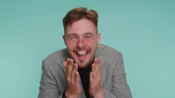 Een geamuseerde zakenman in een jasje wijzend naar de camera, hardop lachend, lachend over belachelijke verschijning, grappige grap. jong guy jongen poseren alleen op blauw studio muur achtergrond - Video