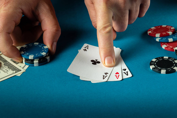 Il giocatore punta con il dito ad una combinazione vincente di tre tipi o set nel gioco del poker su un tavolo blu con fiches e denaro nel club. - Foto, immagini
