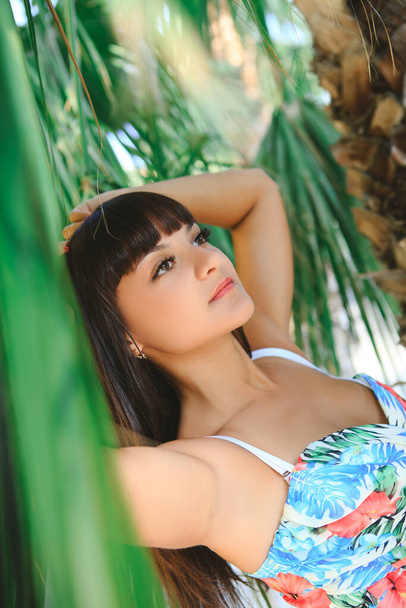 Portrét mladé brunetky s hnědýma očima mezi palmovými listy. Dívka pod palmou za slunečného dne. - Fotografie, Obrázek
