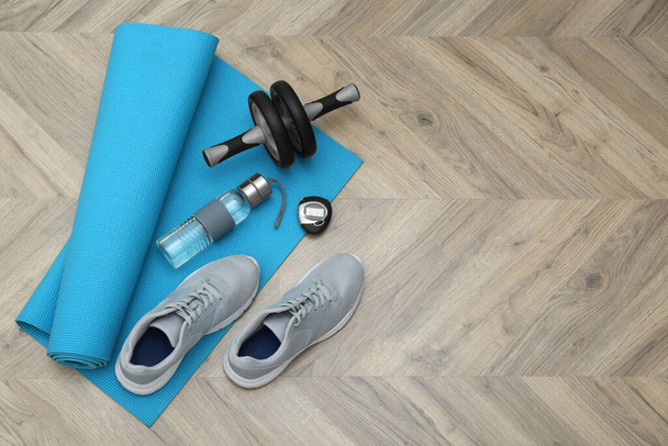 Exercise mat, ab roller, bottle of water, stopwatch and shoes on wooden floor, flat lay. Space for text - Foto, Imagen