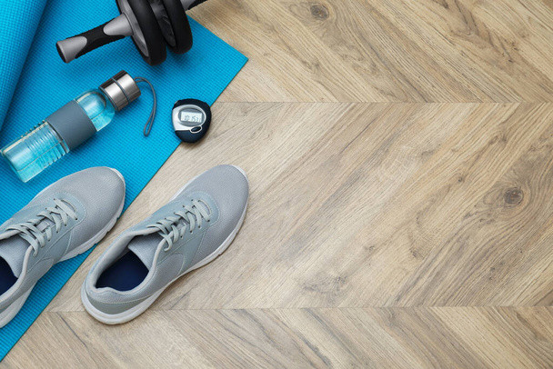 Exercise mat, ab roller, bottle of water, stopwatch and shoes on wooden floor, flat lay. Space for text - Zdjęcie, obraz