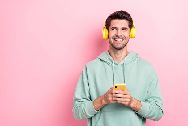 Zdjęcie wesołego pozytywnego człowieka trzymać telefon słuchać muzyki wyglądają puste miejsce odizolowane na różowym tle koloru. - Zdjęcie, obraz