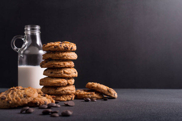 Homemade tasty chocolate chip cookies with glass bottle of milk on dark concrete background - Photo, image
