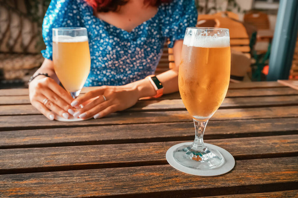 Dziewczyna w pubie lub barze pije chłodne i orzeźwiające świeże światło filtrowane piwo ze szklanek. Pojęcie uroczystości i napojów alkoholowych - Zdjęcie, obraz