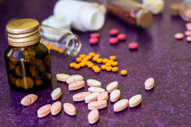 Medical bottles and medication pills spilling out on to purple background - Photo, Image