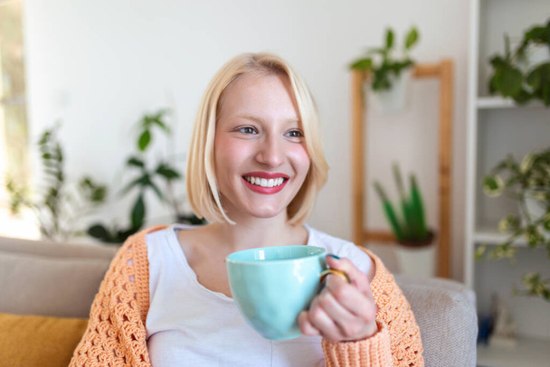 Nahaufnahme einer jungen Frau mit einer Tasse Heißgetränk zu Hause, Leerraum. Menschen, Getränke und Freizeitkonzept - glückliche junge Frau mit Tasse Tee oder Kaffee zu Hause - Foto, Bild