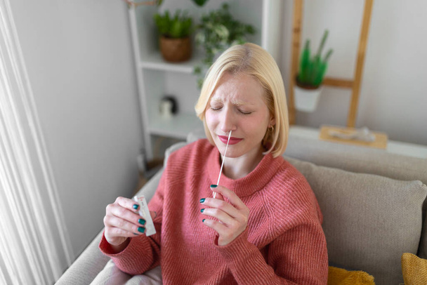 woman using cotton swab while doing coronavirus PCR test at home. Woman using coronavirus rapid diagnostic test. Young woman at home using a nasal swab for COVID-19. - Φωτογραφία, εικόνα