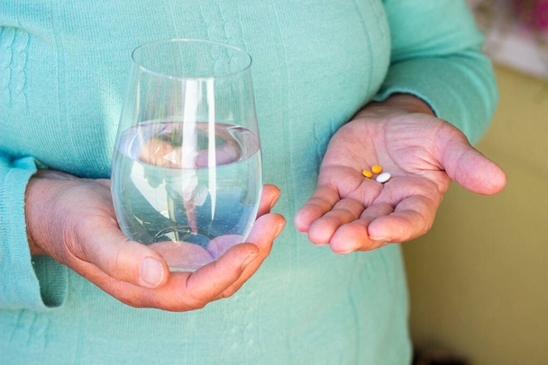 Старшая женщина рука с таблетками лекарства таблетки и стакан воды - Фото, изображение