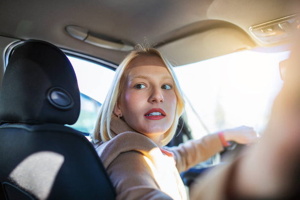 Γυναίκα στο αυτοκίνητο εσωτερική στροφή γύρω κοιτάζοντας τους επιβάτες στο πίσω κάθισμα ιδέα οδηγού ταξί. Έννοια του οχήματος εξετάσεις. Πίσω όψη μιας ελκυστικής νεαρής γυναίκας που κοιτάζει πάνω από τον ώμο της ενώ οδηγεί ένα αυτοκίνητο. - Φωτογραφία, εικόνα