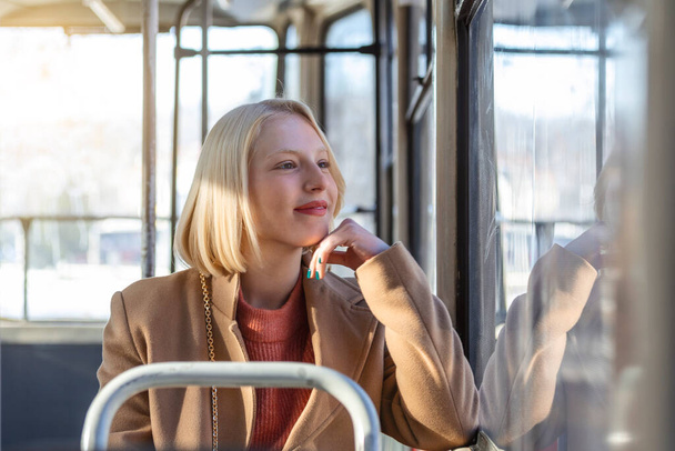 Jedna mladá žena se usmívá v autobuse, zatímco se dívá oknem Krásná mladá žena s autobusem do práce. Cestující v autobuse nebo vlaku, technologie Životní styl, doprava a pojetí cestování. - Fotografie, Obrázek