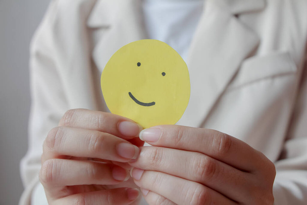 Woman hands holding yellow smile face paper, good feedback rating,think positive, customer review, assessment, world mental health day, Compliment Day. - Foto, afbeelding