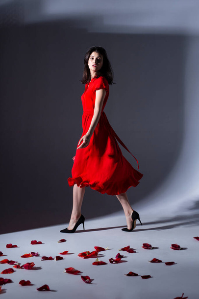 Полное изображение женщины, позирующей в красном платье, держащей букет тюльпанов, позирующей элегантно перед камерой. - Фото, изображение