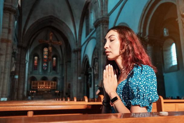 Kız Katolik kilisesinde dua ediyor ve Tanrı 'dan sağlık, günahların affı ve ruhsal huzur için dua ediyor. - Fotoğraf, Görsel