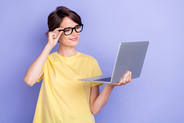 Photo of young attractive pretty gorgeous cute woman wear glasses yellow t-shirt hold new computer positive worker distance nice mood isolated on purple color background. - 写真・画像