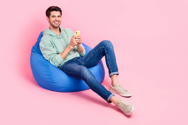 Full length photo of satisfied stylish man sit chair enjoy quality modern device telephone empty space isolated on pink color background. - Foto, Bild