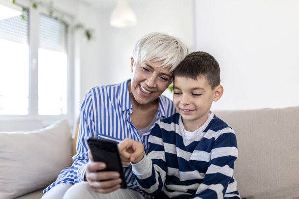 Happy grandmother and grandson using tablet together, sitting on cozy sofa at home, browsing tablet device apps, grandma with grandchild playing game, looking at screen, having fun - Foto, Imagem