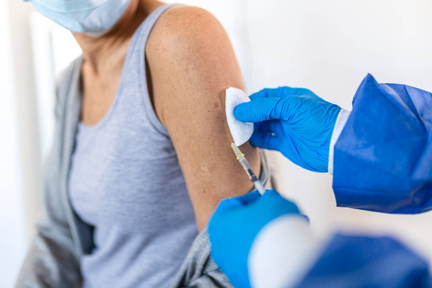 Doctor holding syringe making covid 19 vaccination injection dose in shoulder of female patient wearing mask. Flu influenza vaccine clinical trials concept, corona virus treatment, close up view. - Photo, Image