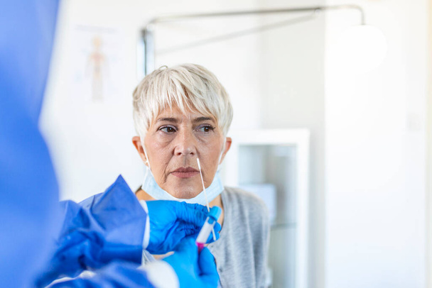 Koronavirüse mi yoksa COVID-19 'a mı yakalandığını belirlemek için koruyucu giysili bir sağlık görevlisi tarafından test edilen klinik ortamdaki olgun beyaz kadın.. - Fotoğraf, Görsel
