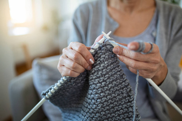 閉じるビューの祖母の手を保持針は彼女の腕で何かを作成ソファの上に座って反復運動編み物を行います。手編みは脳機能を向上させ、古い世代の趣味の概念 - 写真・画像