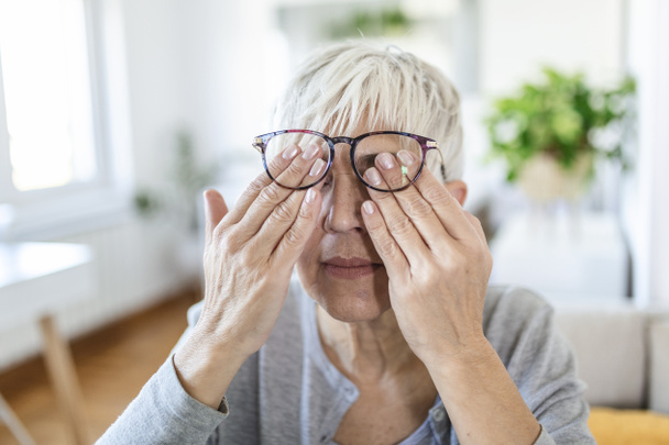 Reife Frau hält Brille mit Dioptriengläsern, reibt sich die Augen und blickt durch sie, das Problem der Kurzsichtigkeit, Sehkorrektur - Foto, Bild