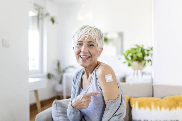 Femme pointant son bras avec un bandage après avoir reçu le vaccin covid-19. Femme mûre montrant son épaule après avoir reçu le vaccin contre le coronavirus - Photo, image