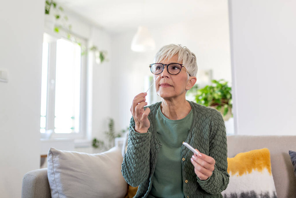 Porträt einer entspannten reifen Frau, die zu Hause einen Selbsttest für COVID-19 macht. Seniorin mit Wattestäbchen beim Coronavirus-PCR-Test zu Hause. Quarantäne, Pandemie. - Foto, Bild