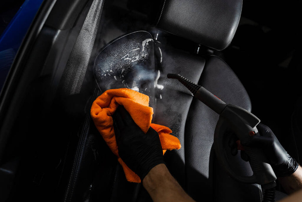 Καθαρισμός ατμού του δερμάτινου καθίσματος μετά το πλύσιμο του αφρού. Εργαζόμενος στην υπηρεσία καθαρισμού αυτοκινήτων καθαρό αυτοκίνητο μέσα. Εσωτερικές λεπτομέρειες αυτοκινήτων - Φωτογραφία, εικόνα