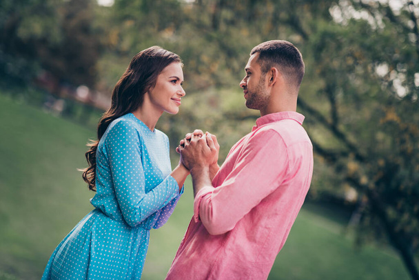 Photo of excited dreamy young husband wife dressed summer clothes holding arms looking eyes outdoors backyard. - 写真・画像