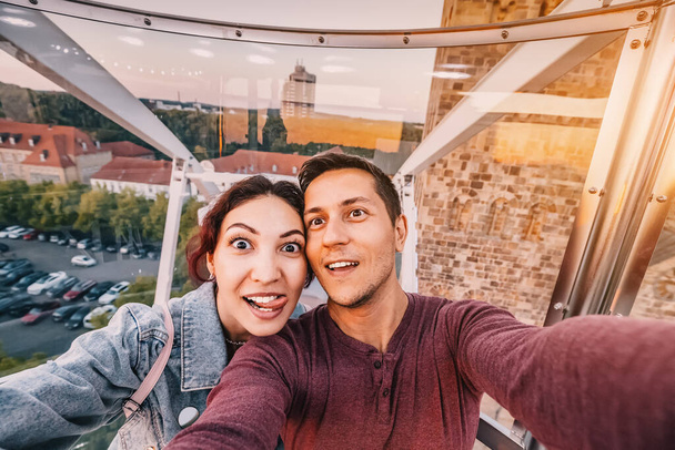 Ένα ερωτευμένο ζευγάρι βγάζει μια selfie φωτογραφία σε ένα περίπτερο με ρόδες Ferris σε ένα κινητό πάρκο διασκέδασης στο κέντρο της παλιάς πόλης του Osnabruck στην Ευρώπη - Φωτογραφία, εικόνα