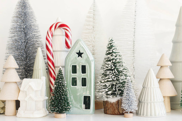 Boldog Karácsonyt és Kellemes Ünnepeket! Stílusos kis karácsonyfák, házak és cukornád fehér asztalon. Modern karácsonyi jelenet, miniatűr ünnepi havas falu. Téli zászló, skandináv dekoráció - Fotó, kép