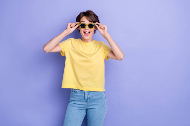 Photo of young adorable gorgeous pretty woman wear yellow t-shirt denim hold new eyeglasses excited sun empty space ad isolated on violet color background. - Фото, изображение